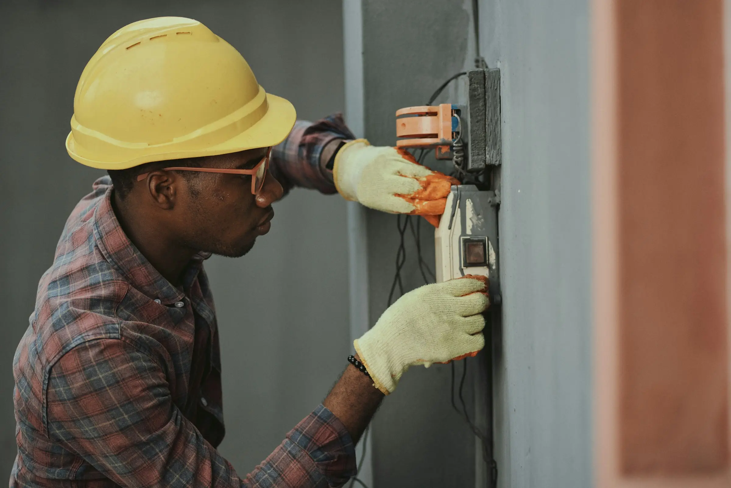 An electrician in a yellow hard hat working on wiring at a wall.