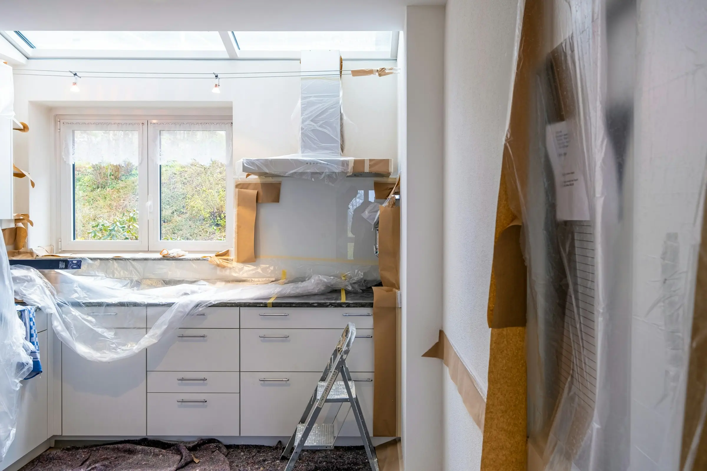 A kitchen in the middle of a renovation, with new white cabinets covered in protective plastic.