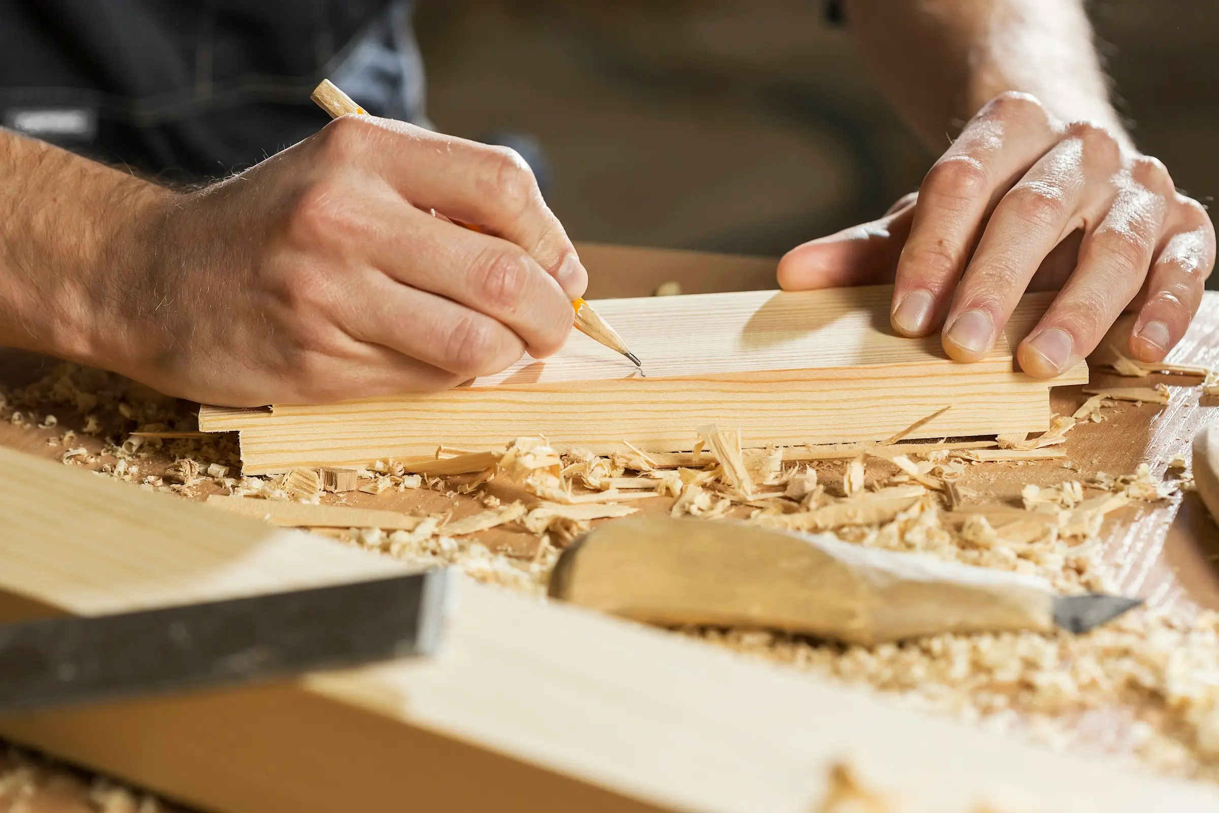 Hands marking a measurement on a wooden board with a pencil.