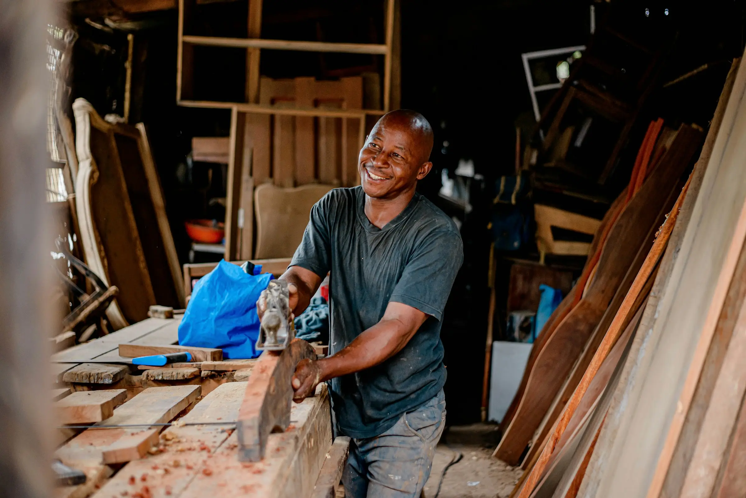 A carpenter smiling as he works on a piece of timber in his workshop.